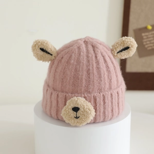 Close-up of pink knitted baby hat featuring cute plush bear ears and cartoon face