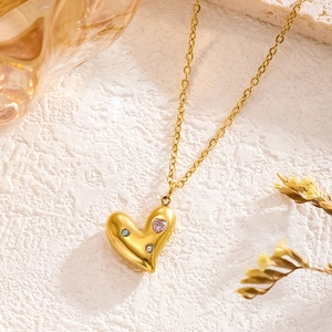 Golden heart pendant necklace with colorful zircon stones on white stone background