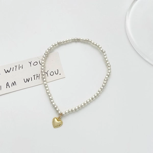 Minimalist silver beaded bracelet with a gold heart pendant on a clean white background