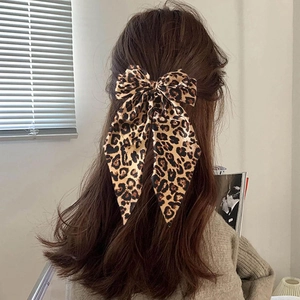 Elegant leopard print bow hair clip with long ribbons worn on wavy brown hair
