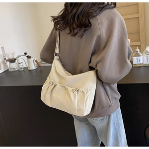 Detailed view of beige nylon crossbody bag worn by a model in a minimalist cafe setting