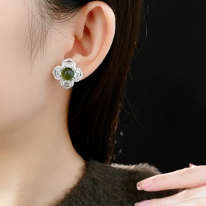 Close-up of green clover flower stud earrings with white zircons on female ear