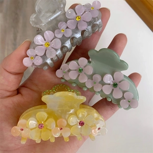 Detailed view of floral acetate hair claws in gray and yellow with sparkling rhinestones