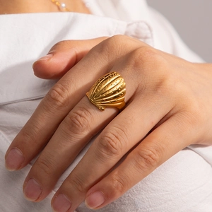Close-up of a gold shell-shaped open ring worn on a finger with a minimalist style