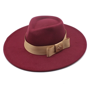Detail of burgundy wool fedora featuring a gold bee ornament on a satin ribbon bow