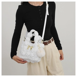 Detail of white quilted bubble fabric handbag featuring a gold bow and plush pom-pom charm