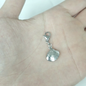 Detailed close-up of a silver shell-shaped pendant with lobster clasp on a palm