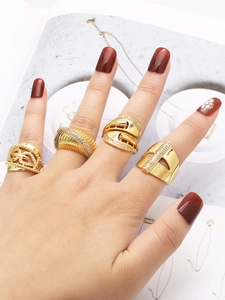 Detail of four gold-plated rings with zircon stones worn by a model over a magazine