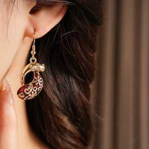 Detailed close-up of a vintage golden drop earring with red enamel and zircon on a model