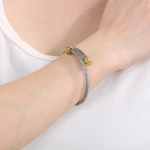 Detail of twisted steel cable bracelet with gold-toned textured accents on wrist