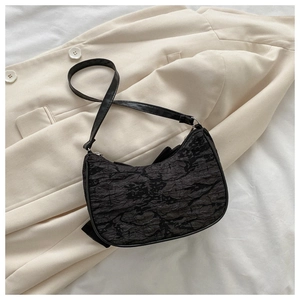 Detail of black pleated crescent bag with textured surface on a beige blazer background