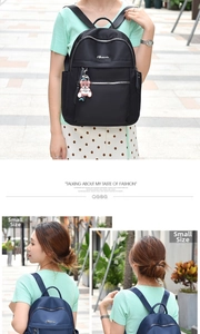 Detail view of nylon backpack with silver zippers and bear charm in black and navy colors