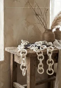 Minimalist white ceramic chain links hanging over a rustic wooden stool in Wabi-sabi style