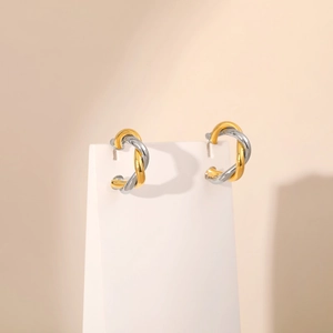 Detailed close-up of twisted two-tone knot earrings on a jewelry stand in gold and silver
