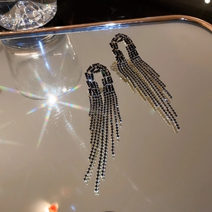 Detail showing dark gothic rhinestone tassel earrings on a metallic tray with light flares