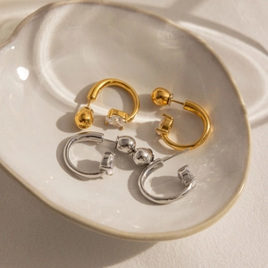 Détail de boucles d'oreilles C en or 18K et argent avec zircon sur plateau céramique
