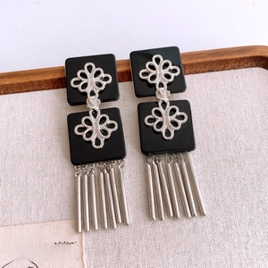 Détail de boucles d'oreilles vintage avec carrés noirs, motifs fleuris et franges