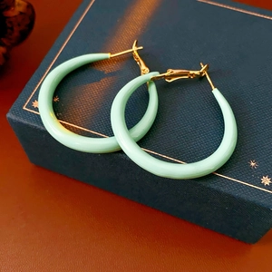 Détail de boucles d'oreilles émaillées vert clair sur un écrin bleu avec touches dorées