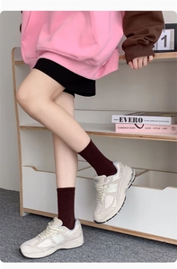 Detail of dark brown ribbed crew socks paired with white mesh sneakers and a hoodie