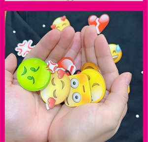 Macro view of glossy acrylic emoji badges with heart and sweat icons on black fabric