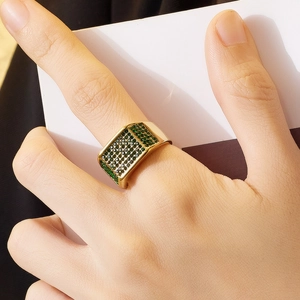 Primo piano di un anello in titanio dorato con zirconi verdi sulla mano del modello
