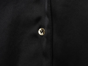 Dettaglio della fibbia in metallo dorato a forma di H su camicia in raso nero