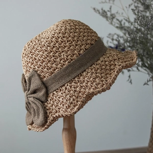 Detail of woven straw sun hat featuring a dark brown bow and textured fiber material