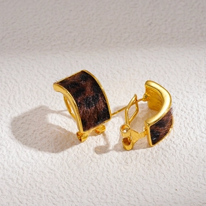 Macro detail of gold C-shaped earrings with faux leopard fur texture and silver pins