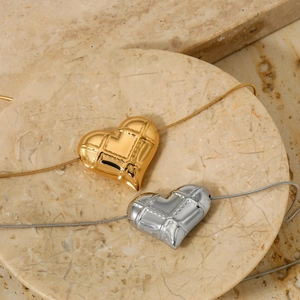 Quilted heart pendant necklace in gold and silver finish on marble tray