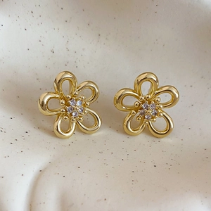 Detailed macro view of gold hollow flower stud earrings with sparkling zircon centers