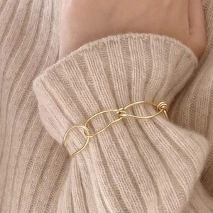 Detail of gold knot chain bracelet on beige knit sweater sleeve with french retro style
