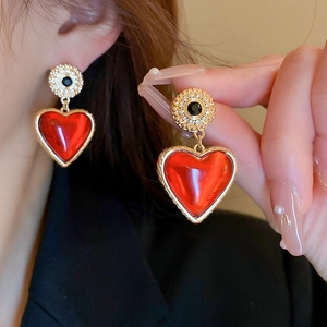Gros plan de boucles d'oreilles cœur rouge vintage avec cadre doré portées par un mannequin