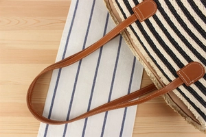 Macro detail of striped woven beach tote bag with brown leather handles and raw frayed edges