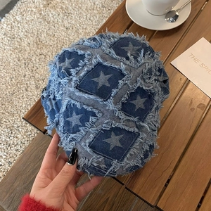 Detail of blue denim beret cap featuring star patch embroidery and frayed tassel edges