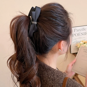 Detailed view of elegant black satin bow hair clip with rhinestones on ponytail