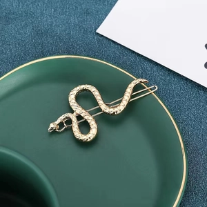 Textured gold snake-shaped metal hair clip displayed on a dark ceramic tray background