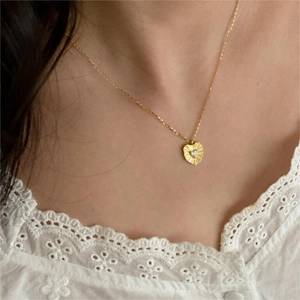 Detail of a gold heart pendant with sunburst texture and zircon on a delicate chain
