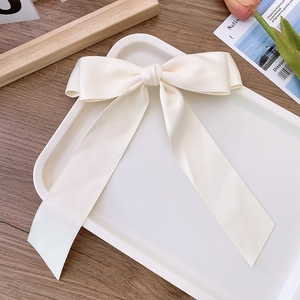 Detailed view of white satin double-layered bow hair clip with ribbons on white tray