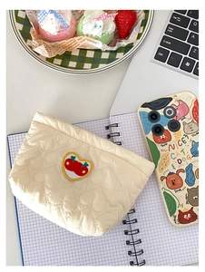 Dettaglio della pochette trapuntata color crema con ricamo a cuore e ciliegia su tessuto