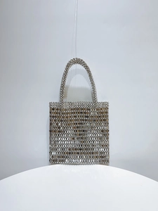 Close-up of a silver sequin woven handbag with chainmail texture and a metal handle