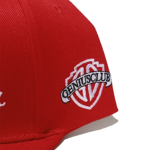 Detail of red twill cotton baseball cap with Genius Club shield embroidery on the side