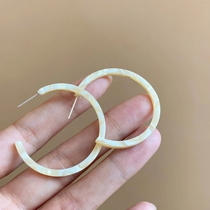 Detail view of large C-shaped resin hoop earrings with cream mosaic texture finish