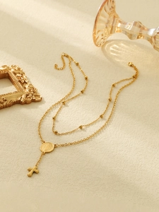 Close-up of double-layered gold cross and Virgin Mary medal necklace with beaded chain