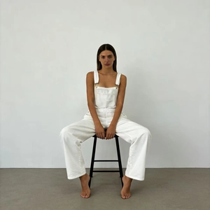 Detail of white denim overalls featuring adjustable metal buckles and loose wide-leg fit