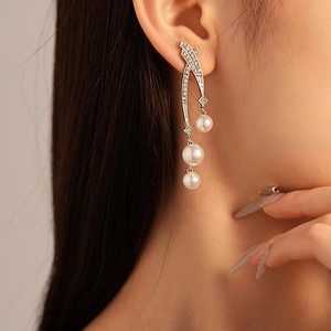 Macro shot of elegant silver cross earrings with shimmering rhinestones and layered pearls