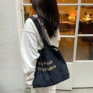 Detail of embroidered gold lettering on a dark blue denim tote bag with soft lighting