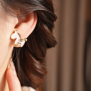 Close-up of golden pony earrings with pearl detail worn on an ear for a stylish look