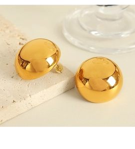 Detail of golden hemispherical stud earrings with polished mirror finish on stone