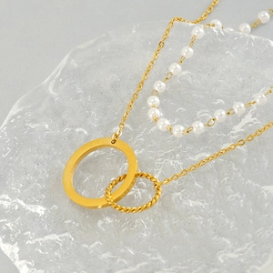 Détail d'un collier double épaisseur doré avec perles et anneaux entrelacés sur verre