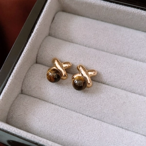 Macro shot of 18k gold plated X-shaped earrings with round tiger eye stone inlay